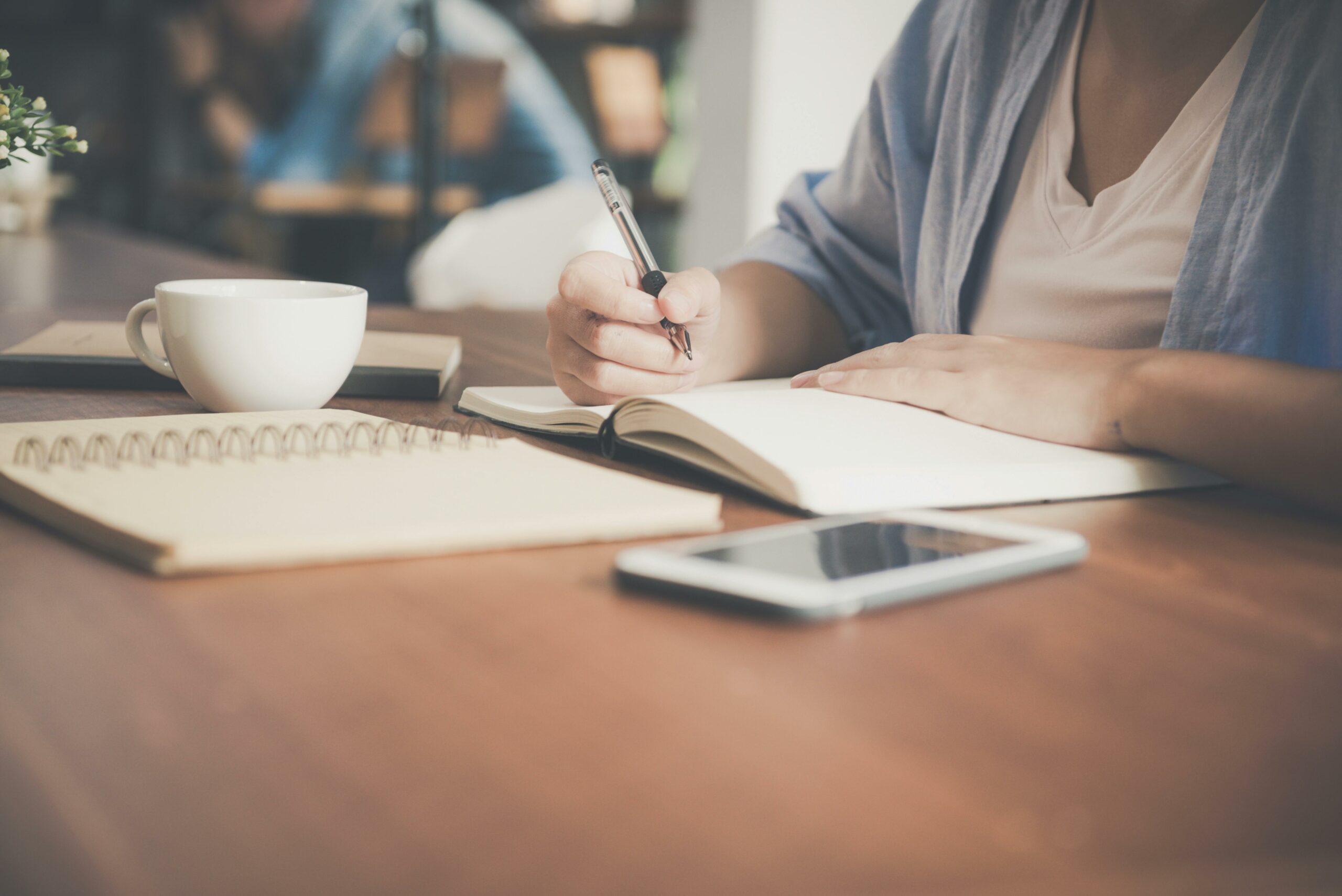 Frau, Die Auf Einem Notizbuch Neben Teetasse Und Tablet Computer Schreibt